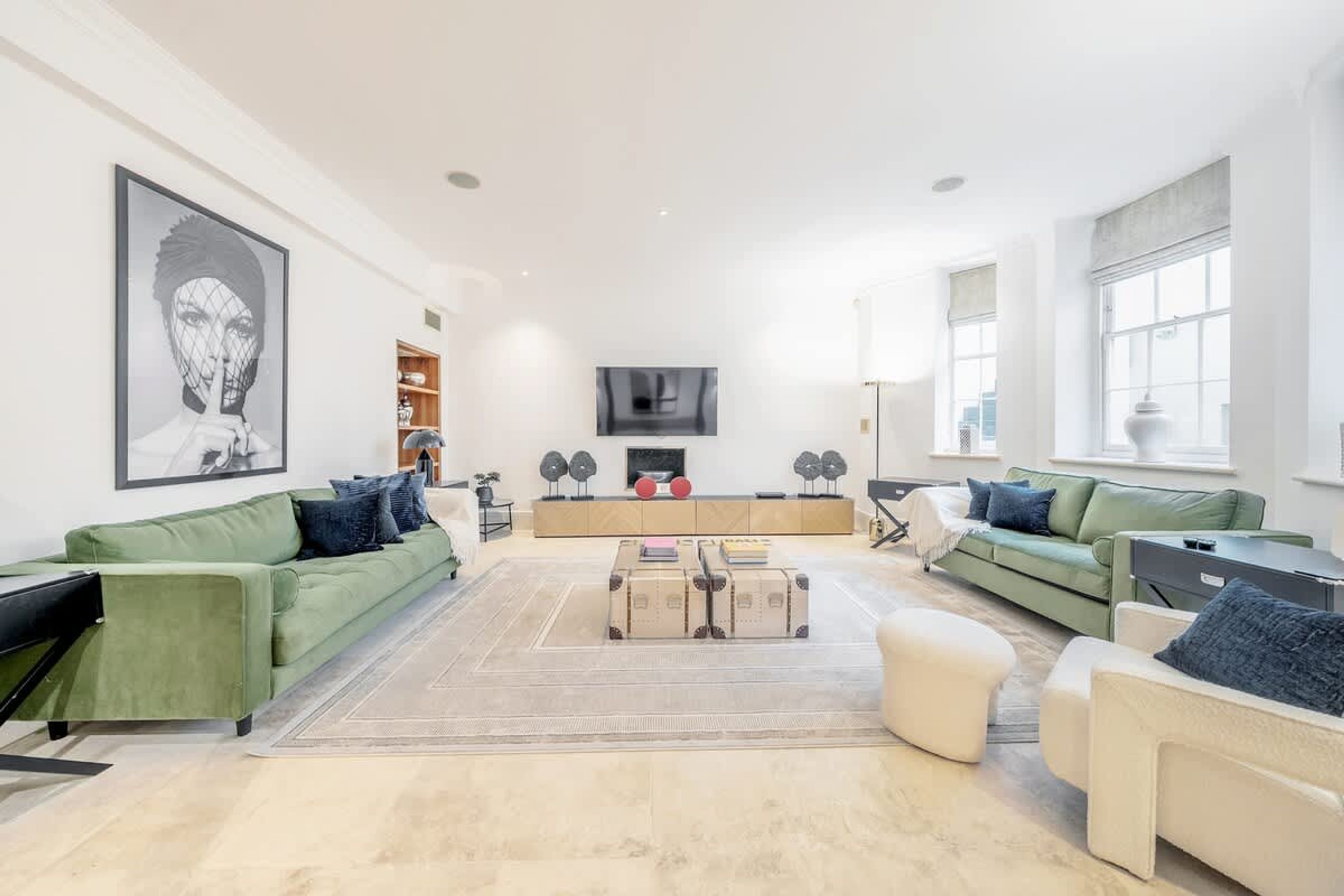 A spacious living room with a green sofa, a white armchair, a coffee table, and a fireplace.
