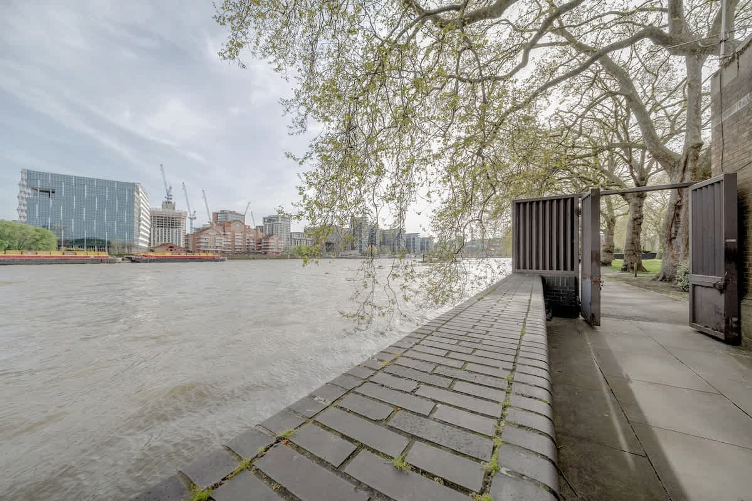 A riverside walkway with a brick path, a wooden fence, and a modern building in the background.