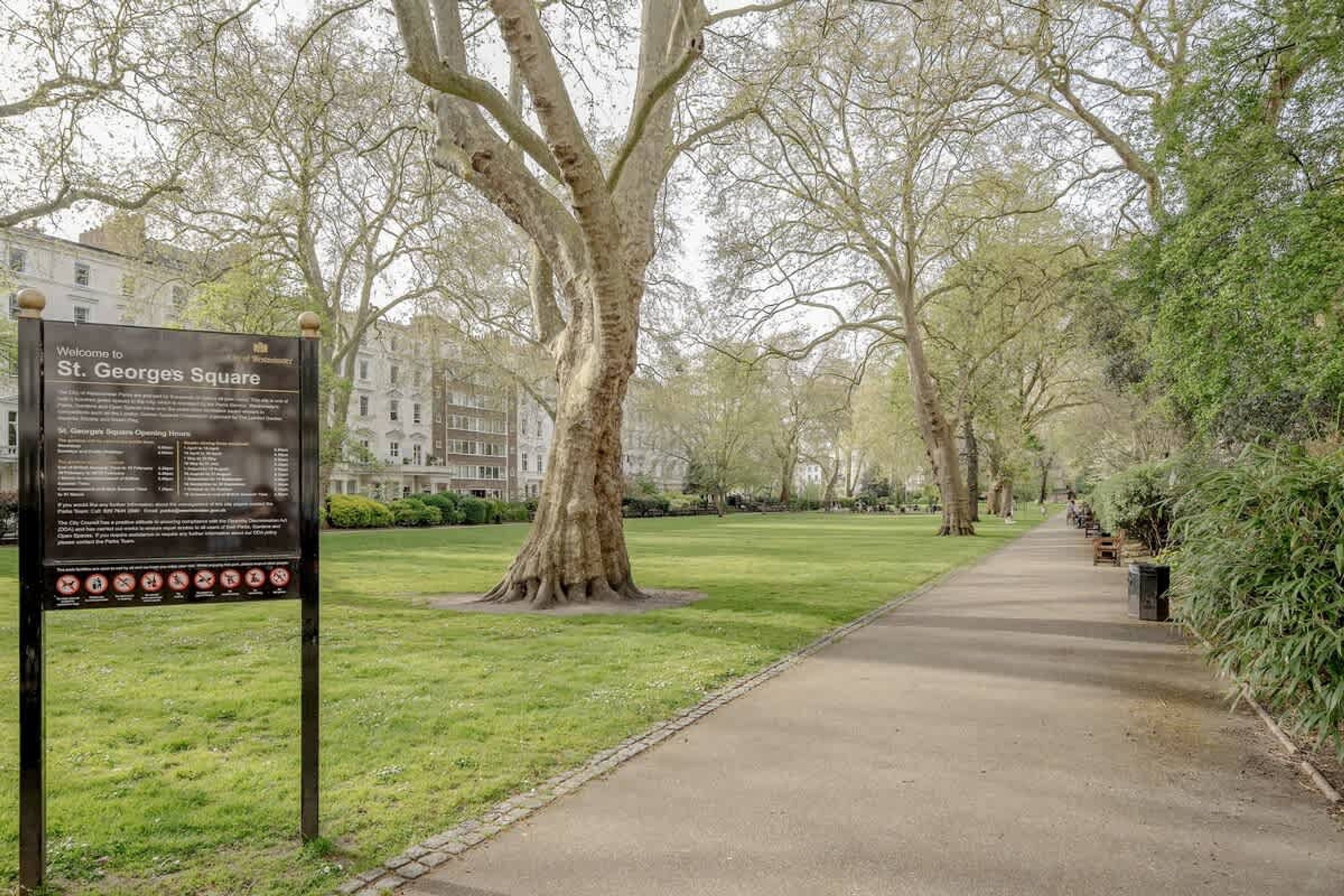 A pathway in St. Georges Square with a signboard, trees, and a building in the background.