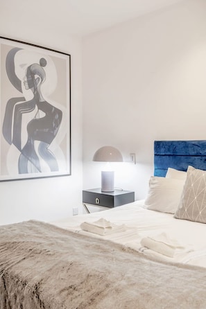 A modern bedroom with a large abstract painting, a blue upholstered headboard, a bedside table with a lamp, and neatly arranged pillows. - Spacious   modern 2bed 2 5bath in Pimlico-Victoria (Greater London)