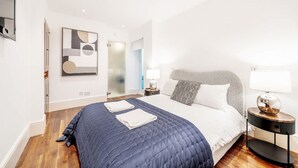 Ein modernes Schlafzimmer mit einem großen Bett, einem Nachttisch mit Lampe und einem abstraktem Kunstwerk an der Wand.