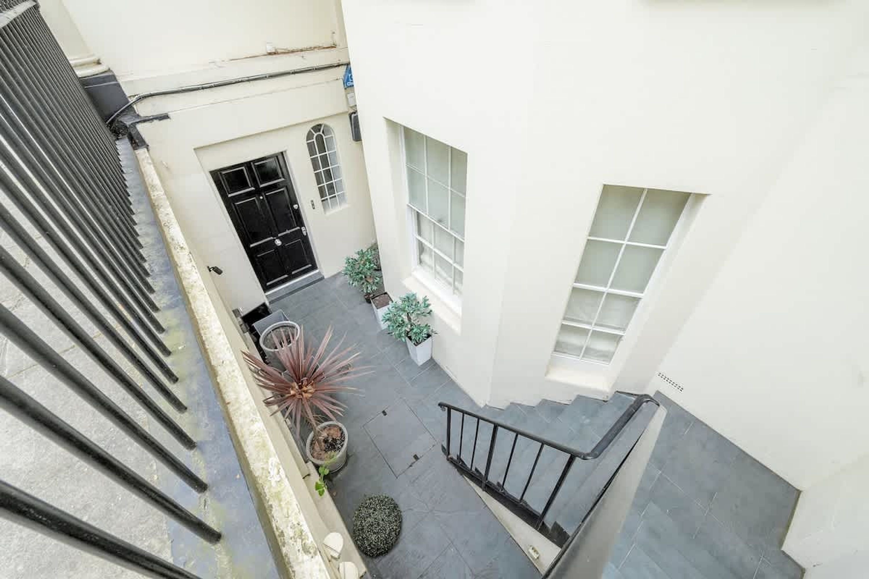 A narrow stairway leading to a landing with a black door and a window. There are potted plants on the landing.