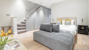 Quarto moderno com cama, sofá cinza, escada e mesa de cabeceira.