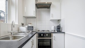 A modern kitchen with white cabinets, a black countertop, a stainless steel sink, a built-in oven, and a coffee maker. - Unbeatable location in Camden-spacious studio flat (Greater London)