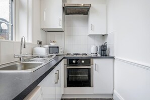 A modern kitchen with white cabinets, a black countertop, a stainless steel sink, a built-in oven, and a coffee maker. - Unbeatable location in Camden-spacious studio flat (Greater London)