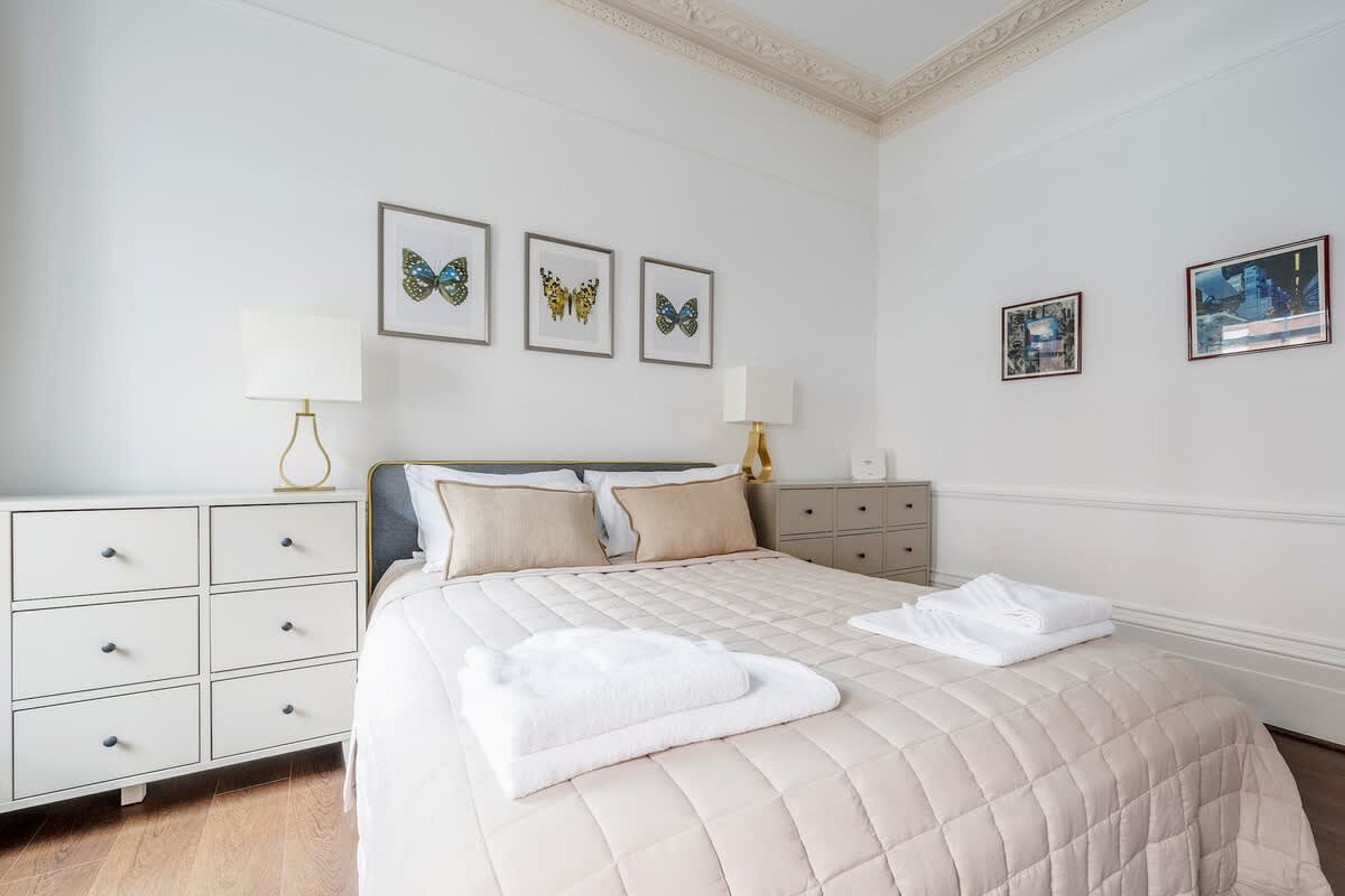 Une chambre à coucher bien rangée, avec un lit, des tables de chevet et des œuvres d’art accrochées au mur.
