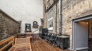 A wooden deck with a table and chairs, a brick wall, and a window. - Unbeatable location in Camden-spacious studio flat (Greater London)