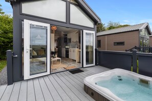 A modern house with a deck, a hot tub, and a kitchen visible through glass doors. - Petite Retreat - Lovely Pod with Hot Tub (Narberth)
