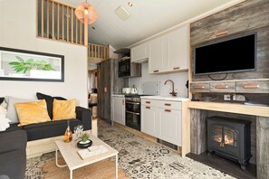 A modern kitchen with white cabinets, a black stove, and a large flat-screen TV mounted above it. - Petite Retreat - Lovely Pod with Hot Tub (Narberth)