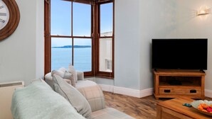 Un salón con un ventanal grande, un televisor de pantalla plana, una mesa de centro de madera y un sofá.
