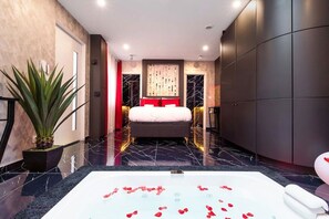 A modern bedroom with a large bed, a bathtub with rose petals, and a potted plant. - Adresse Secrete Suite Spa Prestige avec Balneo (Dijon)