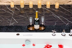 A bathtub with a bottle of champagne and two glasses on a tray, surrounded by candles. - Adresse Secrete Suite Spa Prestige avec Balneo (Dijon)
