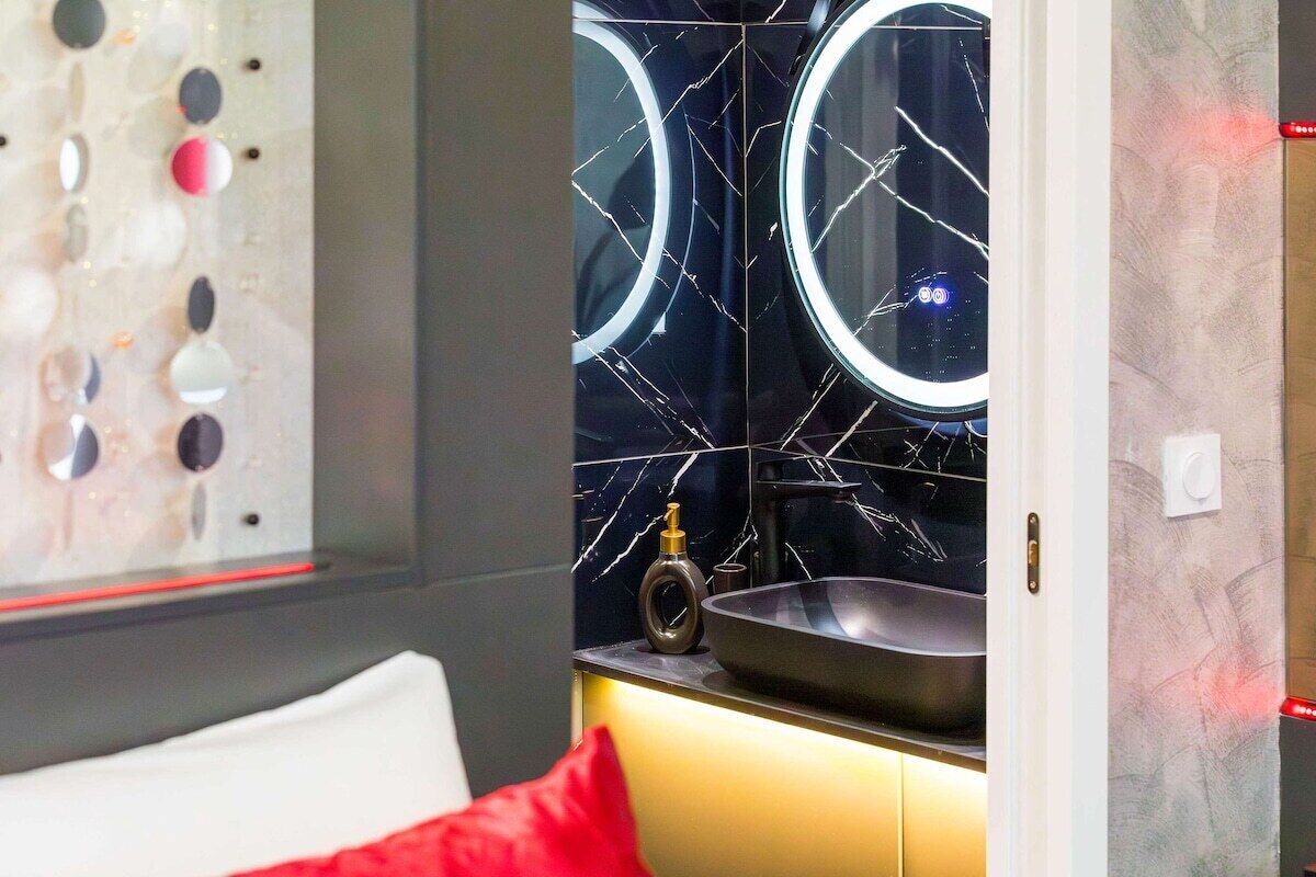 Ein modernes Badezimmer mit schwarzem Marmorfliesenspiegel, einem runden Spiegel und einem Waschbecken.