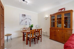 Un coin repas avec une table et des chaises en bois, un meuble avec des portes en verre, un ventilateur et un tableau accroché au mur.
