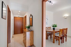 A hallway leading to a dining area with a wooden table and chairs, a potted plant, and a mirror on the wall. - Holiday Home 'Zuri' with Balcony and Wi-Fi (União das freguesias de Conceição e Cabanas de Tavira)