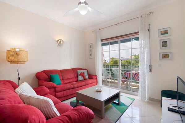 Un salon avec un canapé rouge, une table basse, un téléviseur et un balcon équipé d’une table et de chaises.