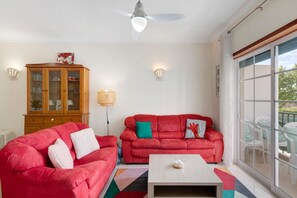 Un salon avec deux canapés rouges, un meuble en bois, une table basse blanche et un ventilateur de plafond.