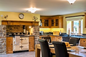 Een keuken met een stenen muur, houten kasten en een eethoek met stoelen en een tafel.