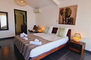 A hotel room with a large bed, a chair, a painting of elephants, and a small table with a lamp. - Villa Rêve Austral - Three Bedroom Villa, Sleeps 6 (Saint Pierre)