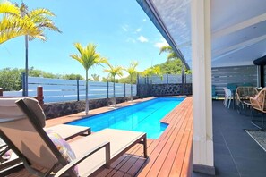 A swimming pool with lounge chairs, a wooden deck, and a stone wall. - Villa Rêve Austral - Three Bedroom Villa, Sleeps 6 (Saint Pierre)