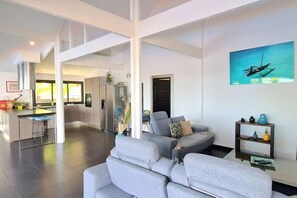 A spacious living area with a grey sofa, a kitchen in the background, and a painting of a boat on the wall. - Villa Rêve Austral - Three Bedroom Villa, Sleeps 6 (Saint Pierre)