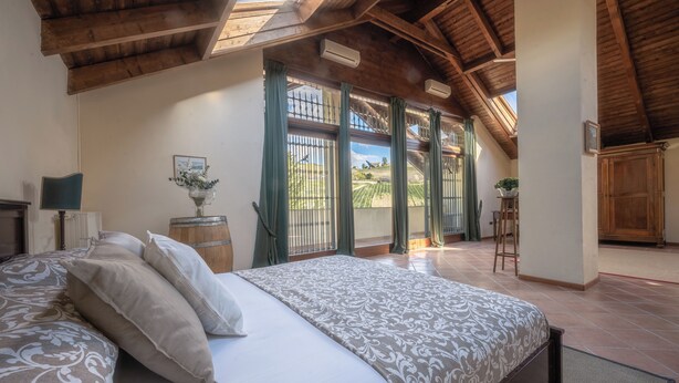 Een slaapkamer met een groot bed, een nachtkastje, een lamp en uitzicht buiten door een raam met gordijnen.