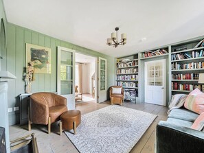 A room with a brown leather chair, a white rug, a bookshelf, and a door leading to another room. - Vosporth Villa (Newquay)