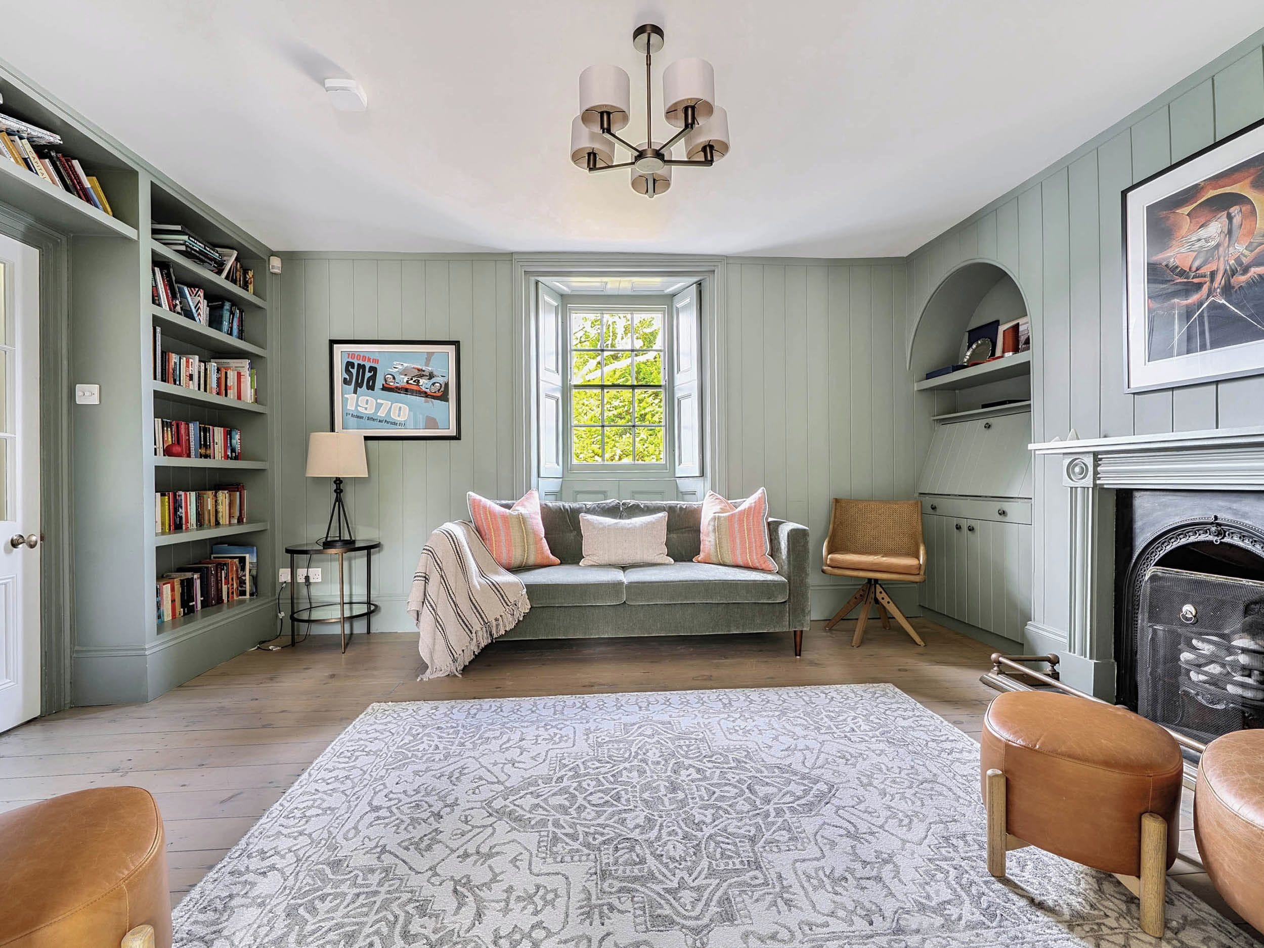 A room with a bookshelf, a sofa, a patterned rug, a chair, and a fireplace.