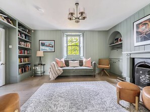 A room with a bookshelf, a sofa, a patterned rug, a chair, and a fireplace. - Vosporth Villa (Newquay)
