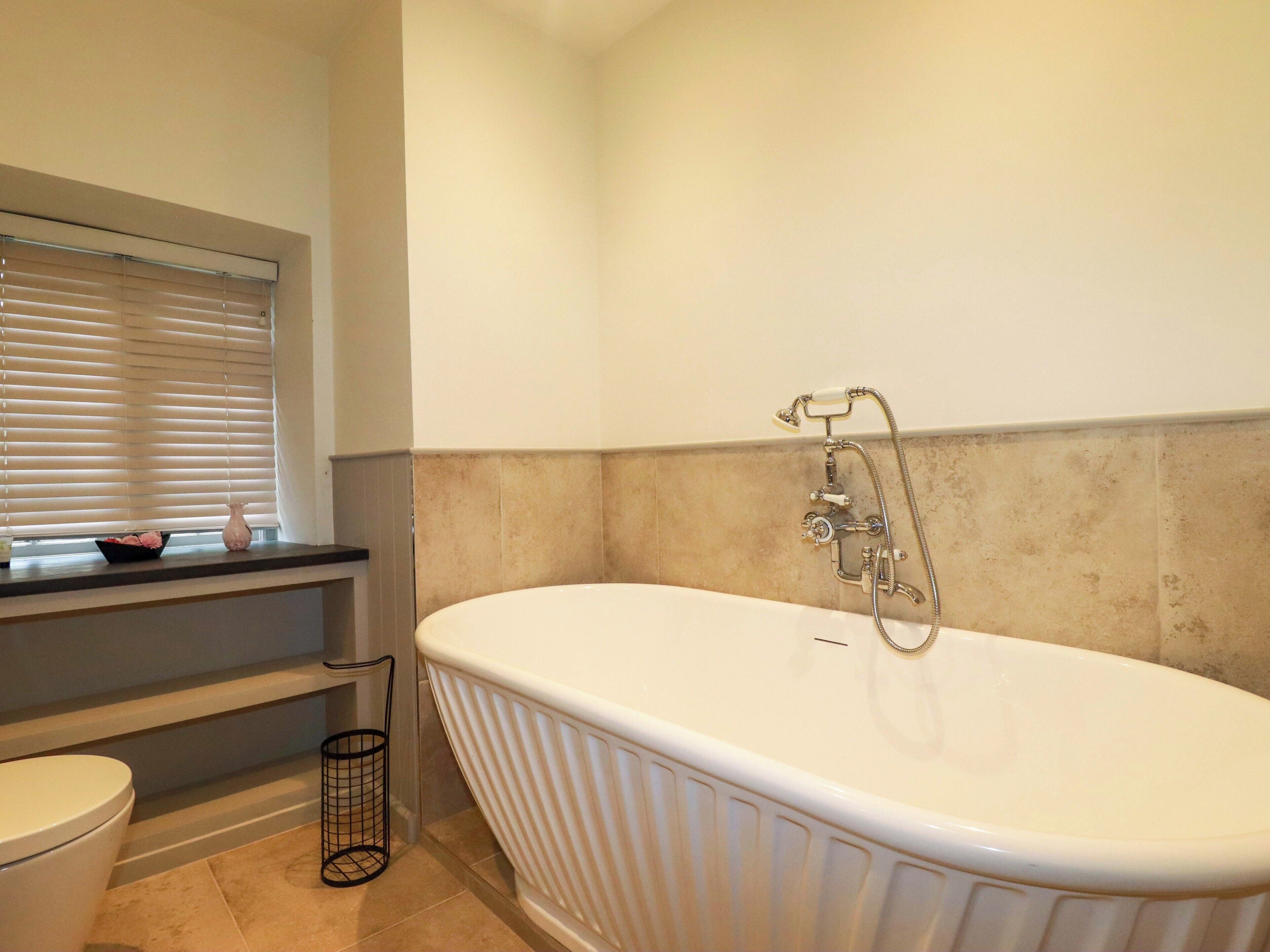 A bathroom with a freestanding bathtub, a toilet, and a window with blinds.