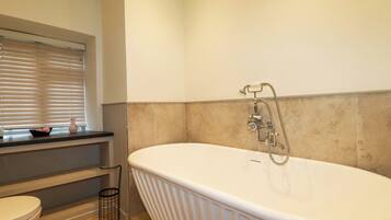 A bathroom with a freestanding bathtub, a toilet, and a window with blinds.