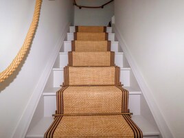 Una escalera con alfombra texturizada y paredes blancas.