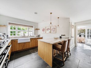 A modern kitchen with wooden cabinets, a marble countertop, and a bar area with stools. - Vosporth Villa (Newquay)