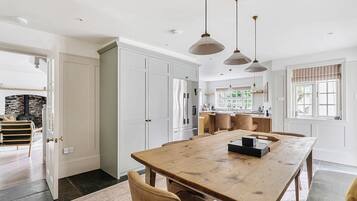 A spacious kitchen with a large wooden table, pendant lights, and a view of the outdoors through a window.