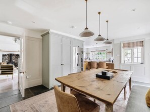 A spacious kitchen with a large wooden table, pendant lights, and a view of the outdoors through a window. - Vosporth Villa (Newquay)