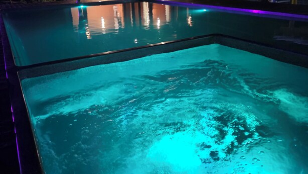 A swimming pool with a clear blue water surface and a wooden deck area.