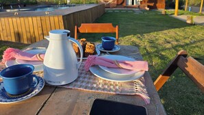A wooden table set with a white coffee pot, blue cups, plates, and a pink napkin.