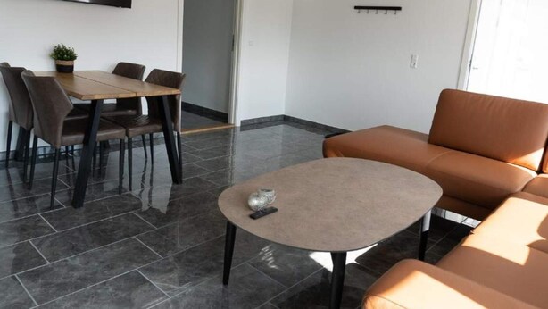 A modern living room with a sofa, a dining table with chairs, and a small round table. - 4 Star Holiday Home in Aabybro (Aabybro)