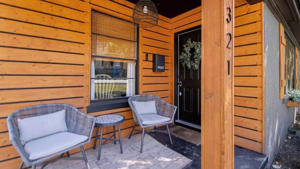 Une cabane en bois avec deux fauteuils en osier et une petite table à l’extérieur, une porte noire avec une boîte aux lettres marquée « POST » et le chiffre « 3 » sur le mur.