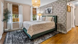 Une chambre à coucher avec un lit, un luminaire suspendu, une fenêtre avec des rideaux, une plante en pot et un papier peint à motifs.