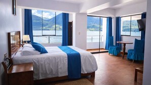 Une chambre d’hôtel avec un grand lit, un bureau, une chaise et une vue sur un lac et des montagnes.