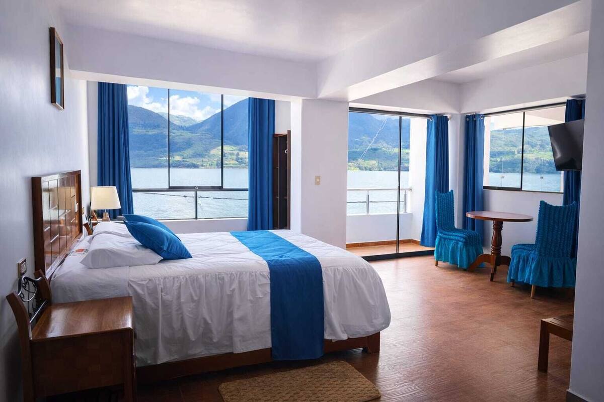 Une chambre d’hôtel avec un grand lit, un bureau, une chaise et une vue sur un lac et des montagnes.