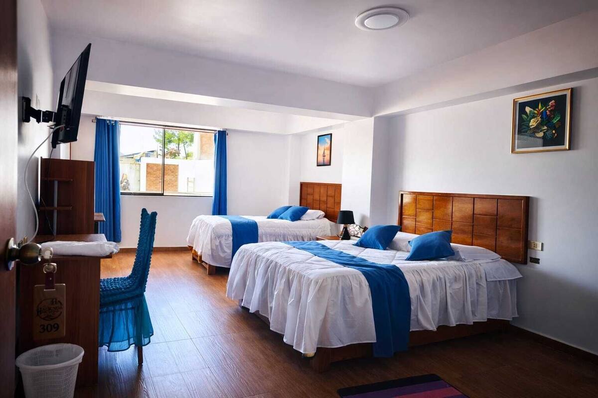 Une chambre d’hôtel avec deux lits, une télévision, une fenêtre avec des rideaux, un plancher en bois et un tableau au mur.