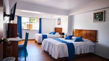 A hotel room with two beds, a TV, a window with curtains, a wooden floor, and a painting on the wall.