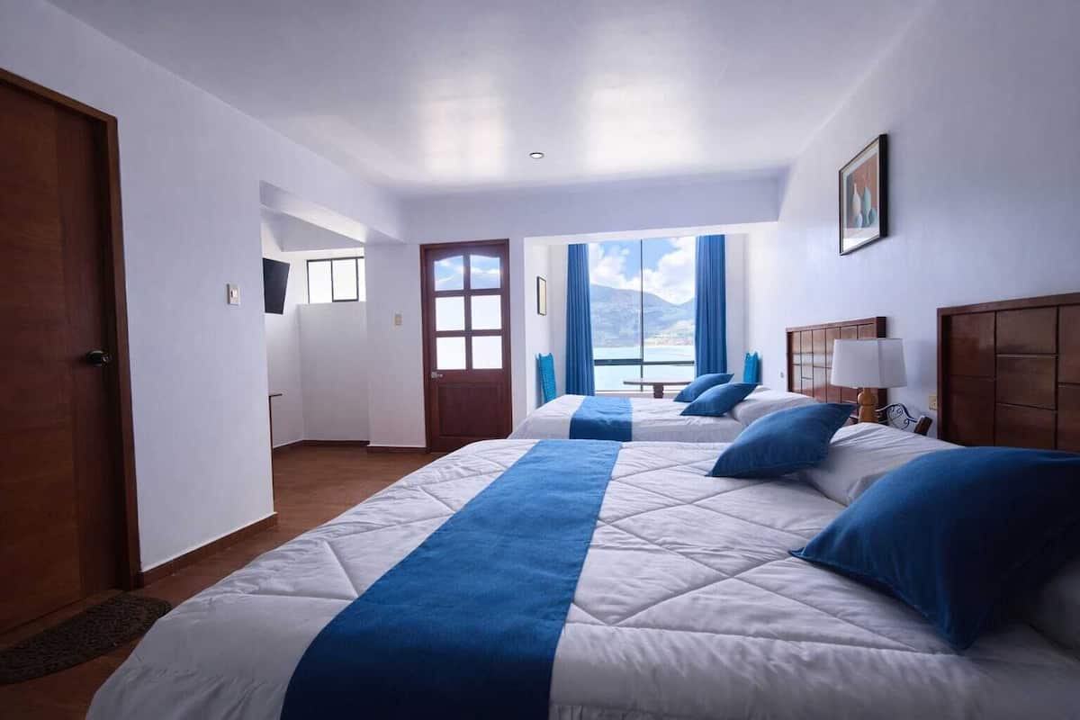 Une chambre d’hôtel avec un grand lit, une tête de lit en bois, une table de chevet avec une lampe et une vue sur l’extérieur par une fenêtre.