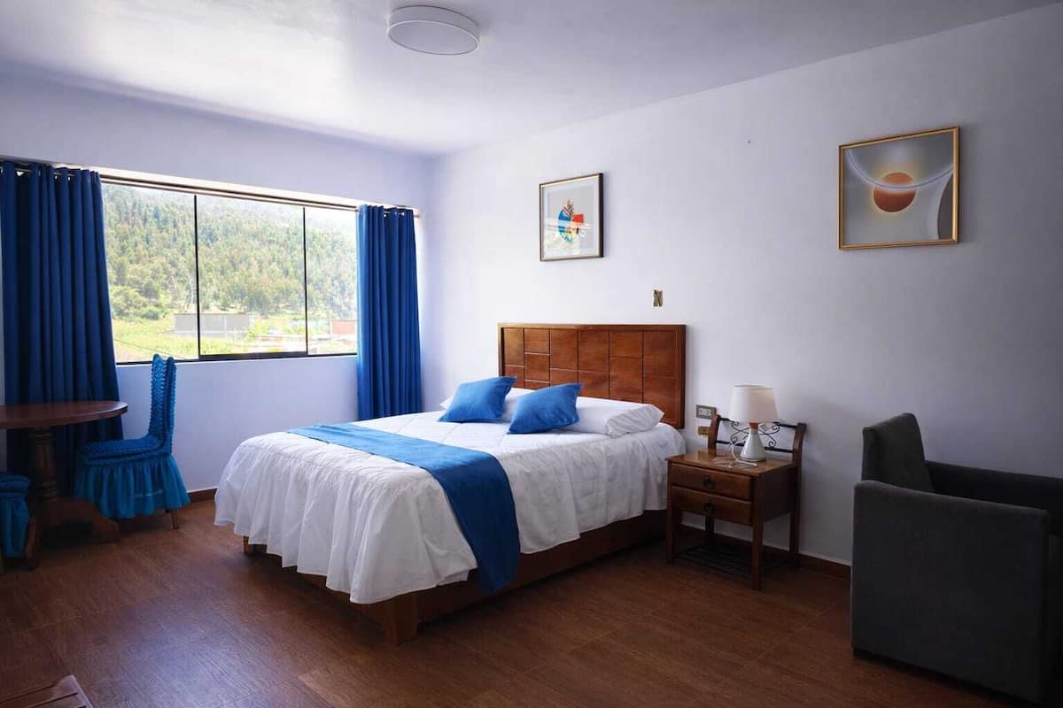 Une chambre à coucher bien rangée, avec un lit en bois, des rideaux bleus, une petite table et une chaise.