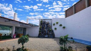 Une cour intérieure avec un mur en pierre, un élément décoratif aquatique et des plantes en pot.