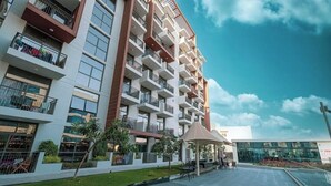A multi-story residential building with balconies, a covered outdoor seating area, and a landscaped garden. - Stylish Studio with Balcony & Pool View in Arjan – Close to Miracle Garden (Dubai)