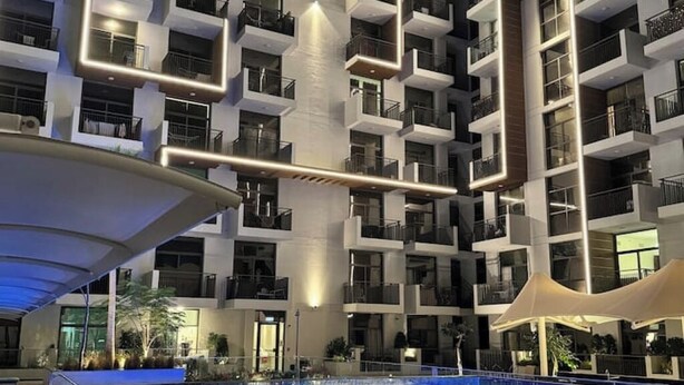 A modern hotel with a rooftop pool, multiple balconies, and a contemporary design. - Stylish Studio with Balcony & Pool View in Arjan – Close to Miracle Garden (Dubai)