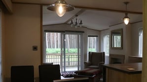 A dining area with a wooden table and chairs, a bench, and a kitchen area with a counter and chairs. - Living The Dream (Holt)